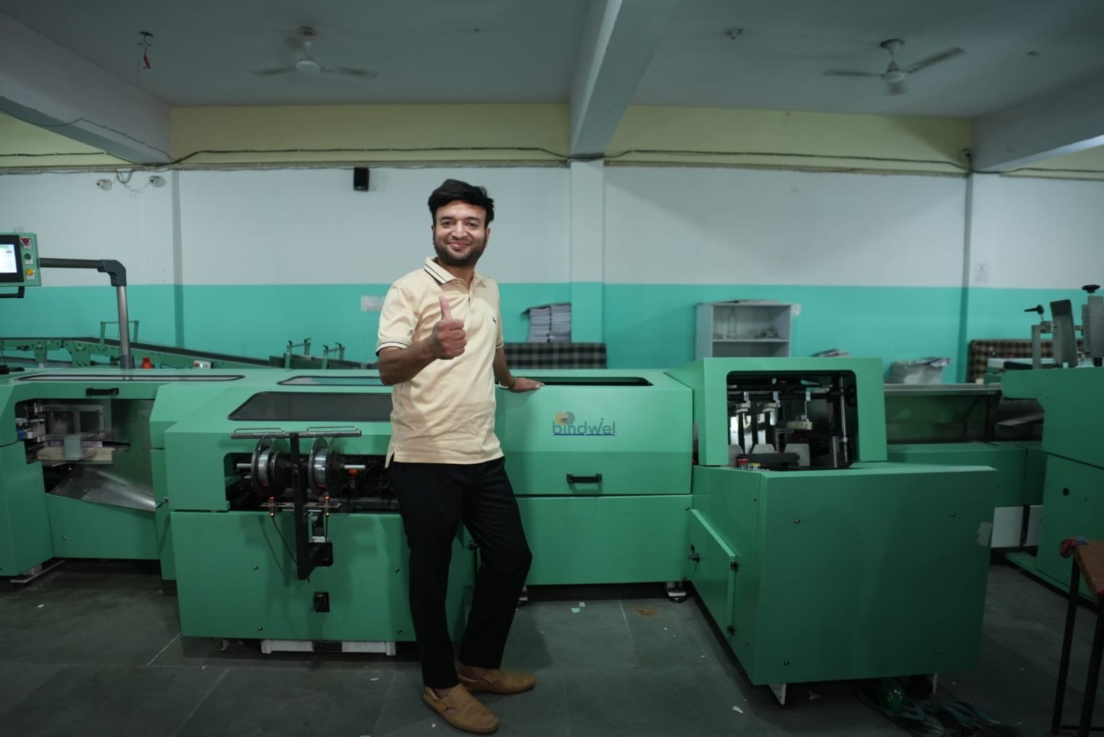 Team member giving a thumbs-up beside a green Bindwel binding machine