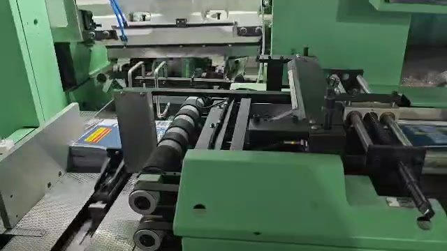 A green binding machine feeding books onto a conveyor